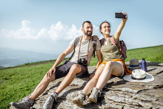 Young couple having fun, making selfie photo with phone while hiking in the mountains during the summer time