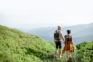 Beautiful couple walking with backpacks on the green meadow, while traveling high in the mountains...