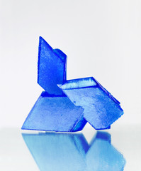 Blue crystals of copper sulfate on mirror surface on white background