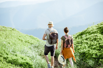 Beautiful couple walking with backpacks on the green valley, while traveling high in the mountains...