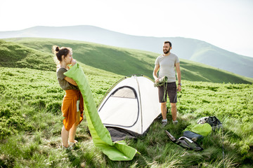Young couple setting up the tent and inflating the mattress on the green meadow, traveling high in the mountains during the sunset © rh2010