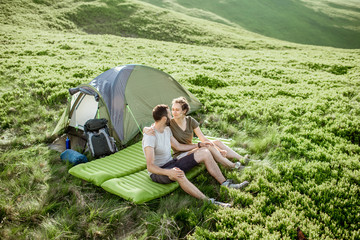 Young lovely couple sitting together on the mattress at the campsite, enjoying summer time while traveling in the mountains