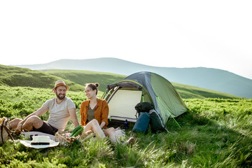 Young and cheerful couple having a picnic at the campsite while traveling high in the mountains...