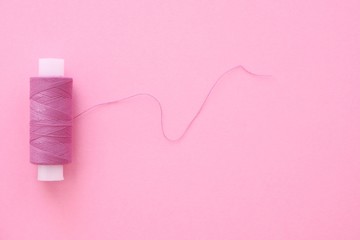 One spool of lilac (pink, violet, crimson) sewing thread on a pink paper backgroun, copy space for text. Top view, flat lay.