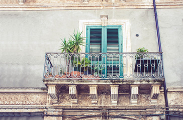 Fototapeta na wymiar Balcony with flowerpots and house palm plants in a historic building in Catania, traditional architecture of Sicily, Italyю