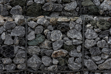 Close-up of a retaining wall made of stones. A wall called a gabion. Stone wall with metal grid as background.