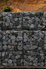 Retaining stone wall next to the road. Protection fence or wall made of gabions with stones. Stone wall with metal grid as background. stone floor texture, A wall called a gabion.