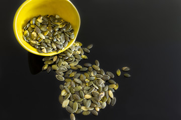 bowl of pumpkin seeds spilled on the black table.