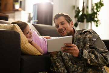 Happy military father and daughter using digital tablet at home.