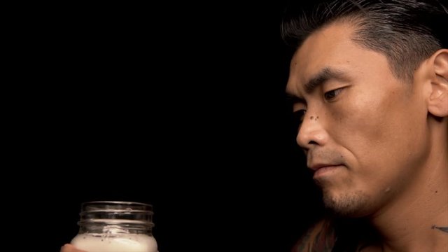 This slow motion video shows a profile view of an asian man drinking and chugging beer from a mug against a black background.