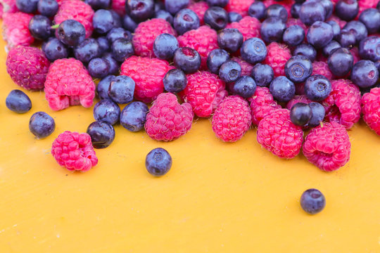 Fresh and juicy wild berries of raspberry and blueberry on a yellow background