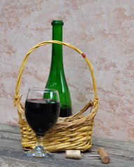 Still life with an open bottle of red wine, a glass and a basket.
