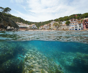 Spain coastal village with beach and fish underwater, Mediterranean sea, Sa Tuna cove, Begur, Costa Brava, Catalonia, split view half over and under water