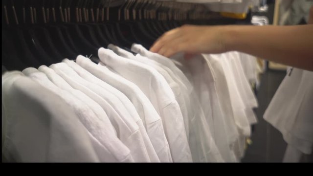 the girl examines the white t-shirts on hangers in the store alternately shifting them. The concept of free time. Close up.