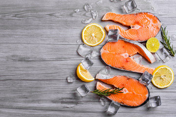 Salmon steaks on ice with lemon and rosemary on dark wooden table top view. Fish food concept. Copy space