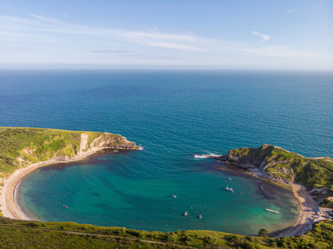 A view of the Lulworth Cove along the Jurrassic Coast in Dorset under a majestic blue sky and some white clouds.