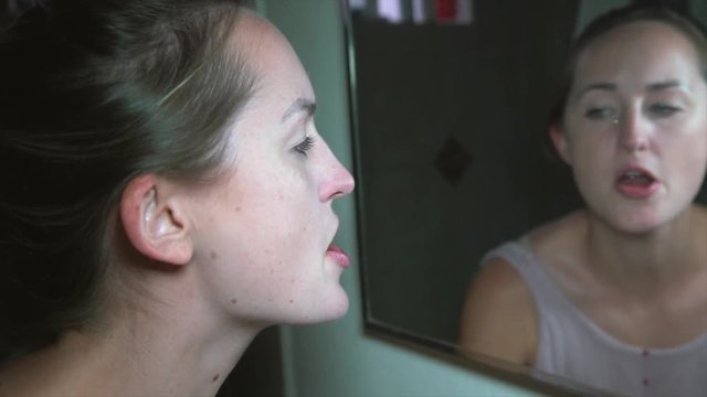 This video shows a sick and troubled young woman looking into a dirty bathroom mirror and spitting blood.