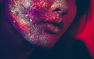 Beautiful young woman dancing and making party with fluorescent painting on her face. Neon facial...