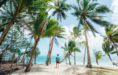Plakat Man standing on the beach and enjoying the tropical place with a view. caribbean sea colors and palm trees in the background. Concept about travels and lifestyle
