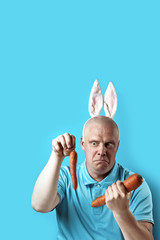 Bald brutal man in light t-shirt and rabbit ears. In his hands he holds the carrot of a different size.