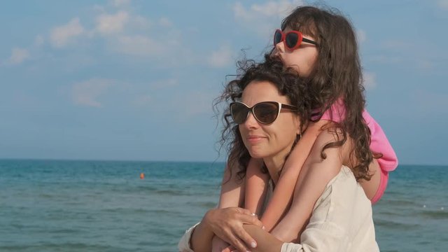 Portrait of a happy mother with a child. A little daughter sits on her mother's shoulders against the backdrop of the sea.