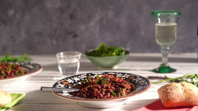Low angle turn left focussed on bowl of red beans and kale in italian setting with champagne or prosecco.
