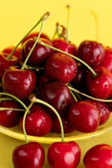 Freshly picked cherries in a glass bowl. Bright yellow background, water drops, high resolution