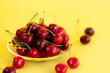 Obraz na płótnie Canvas Freshly picked cherries in a glass bowl. Bright yellow background, water drops, high resolution