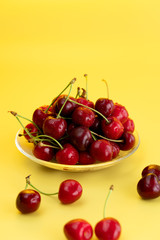 Freshly picked cherries in a glass bowl. Bright yellow background, water drops, high resolution