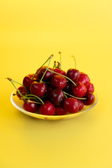 Freshly picked cherries in a glass bowl. Bright yellow background, water drops, high resolution