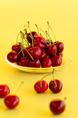 Freshly picked cherries in a glass bowl. Bright yellow background, water drops, high resolution