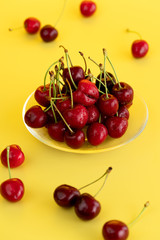 Freshly picked cherries in a glass bowl. Bright yellow background, water drops, high resolution