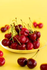 Freshly picked cherries in a glass bowl. Bright yellow background, water drops, high resolution