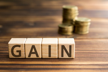 inscription gain wooden cubes with letters, money piles of coins,  wooden background