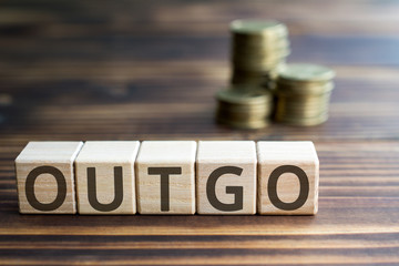 inscription outgo wooden cubes with letters, money piles of coins,  wooden background