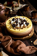 Beautiful still life with homemade delicious three chocolates cheese cake on wooden stand on rustic table