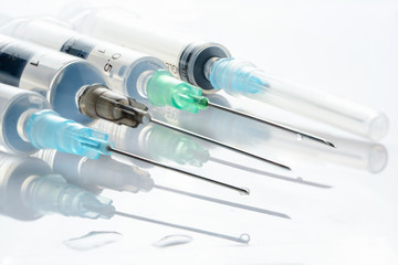 Four syringes with medicinal solution, on white background with reflection and water drops. 2 and 5...