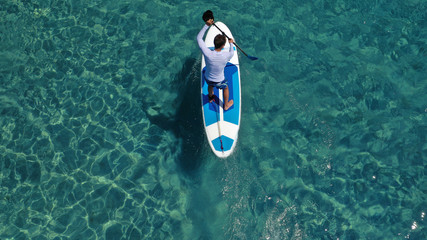 Aerial drone photo of unidentified fit man practising Stand Up Paddle or SUP in tropical exotic...