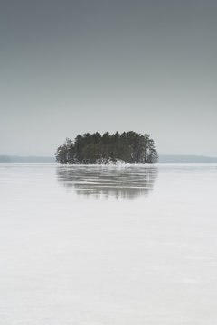 Small island reflecting on winter frozen lake