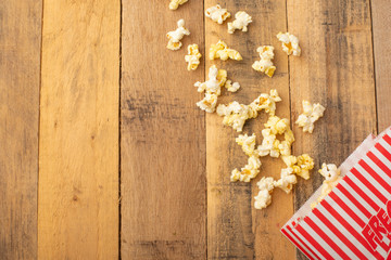 packaging with popcorn on a wooden background. sprinkled popcorn. rest and entertainment. background