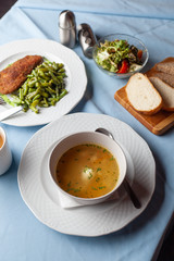 Three course substantial set meal on a blue tablecloth: hot chicken noodle soup, chicken schnitzel with green beans green broccoli salad and a cup of coffee