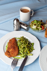 Deep fried chicken schnitzel with crunchy crust and steamed green beans, served with vegetable green salad and tomatoes for a nutritious lunch