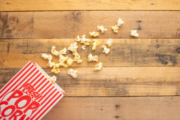 packaging with popcorn on a wooden background. sprinkled popcorn. rest and entertainment. background