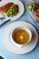 Three course substantial set meal on a blue tablecloth: hot chicken noodle soup, chicken schnitzel with green beans green broccoli salad and a cup of coffee
