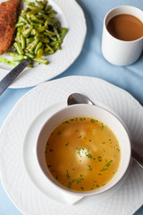 Three course substantial set meal on a blue tablecloth: hot chicken noodle soup, chicken schnitzel with green beans green broccoli salad and a cup of coffee