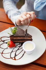 Woman is eating a big piece of chocolate Prague cake with glaze, buttercream and chocolate topping with a small spoon, cutting it in pieces