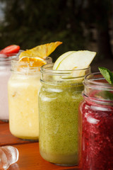 Close up view of different tastes of smoothies on a wooden table: strawberry, apple green, citrus and berries smoothies