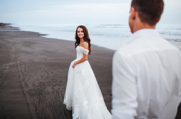 Elegant gorgeous bride and groom walking on ocean beach during sunset time. Romantic walk newlyweds on tropical island. Concept marriage, just married