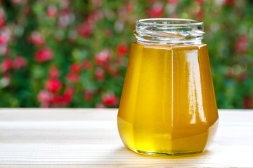 Jar of organic floral honey with a drizzle against flowers background . Outdoor.