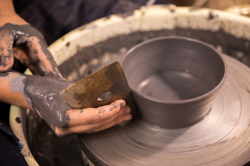 Womens hands at work on a potters wheel with black clay